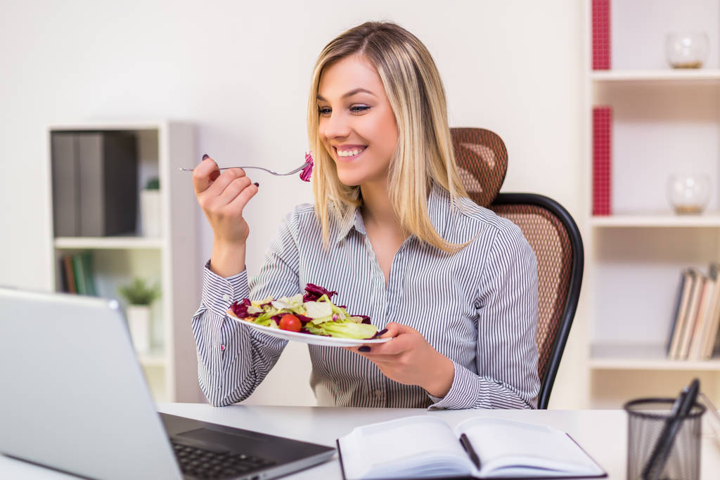 Belle femme d'affaires aime manger de la salade tout en travaillant dans son bureau
. - Photo, image
