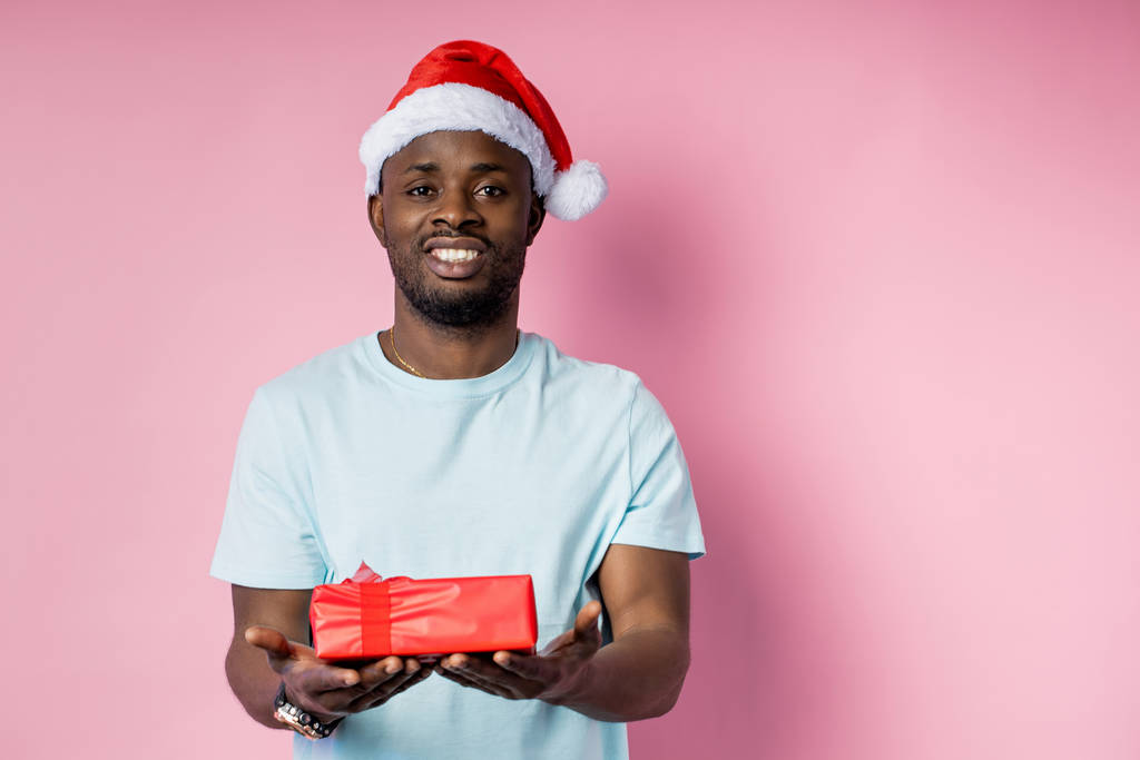 Young african american man wearing Santa hat holding gift - Photo, Image