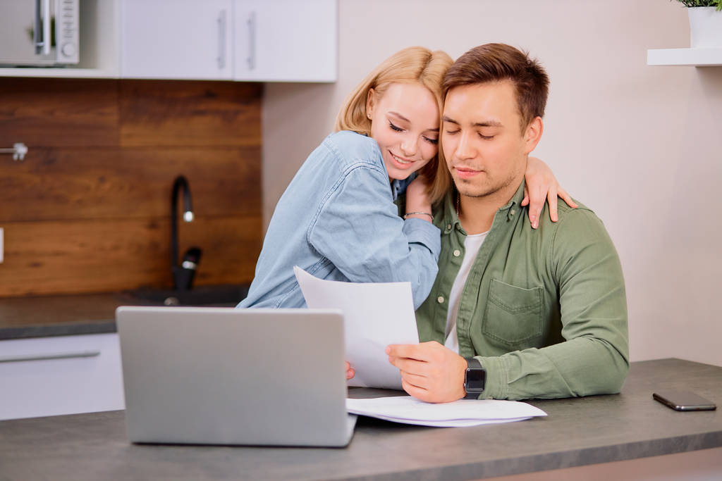 счастливая пара в доме с современным ноутбуком, семья рассматривает ипотеку или страховку
 - Фото, изображение