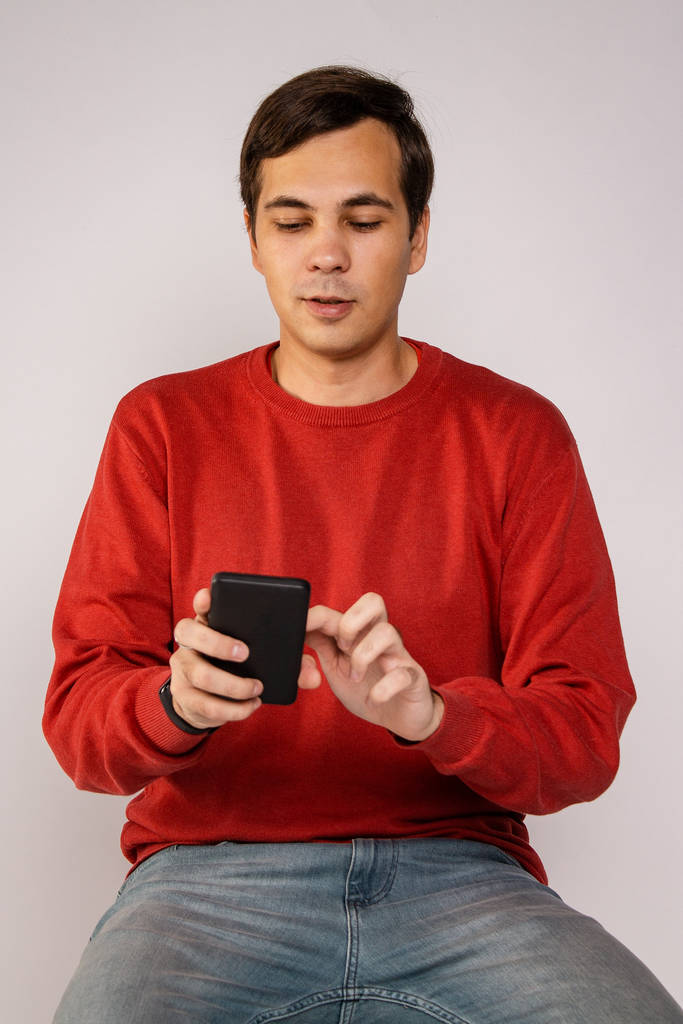 Ten chlap v červeném svetru používá smartphone. Prozkoumá obrázek - Fotografie, Obrázek