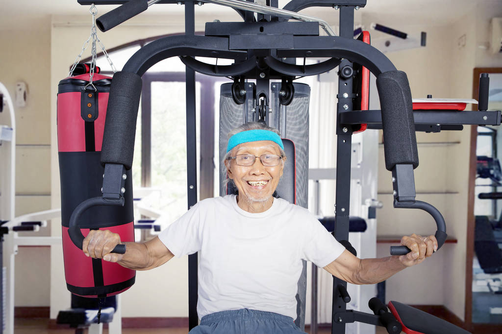 Ο γέρος Ασιάτης γυμνάζεται στο γυμναστήριο με γυαλιά. - Φωτογραφία, εικόνα