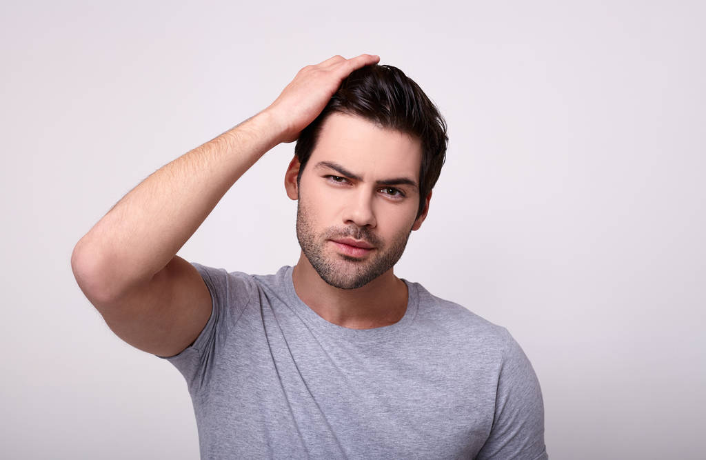 Um jovem branco em uma camiseta cinza corrige seu corte de cabelo
. - Foto, Imagem