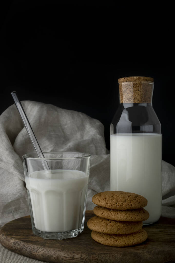 Egy pohár tej, egy üveg tej és zabkeksz a vágódeszkán. - Fotó, kép