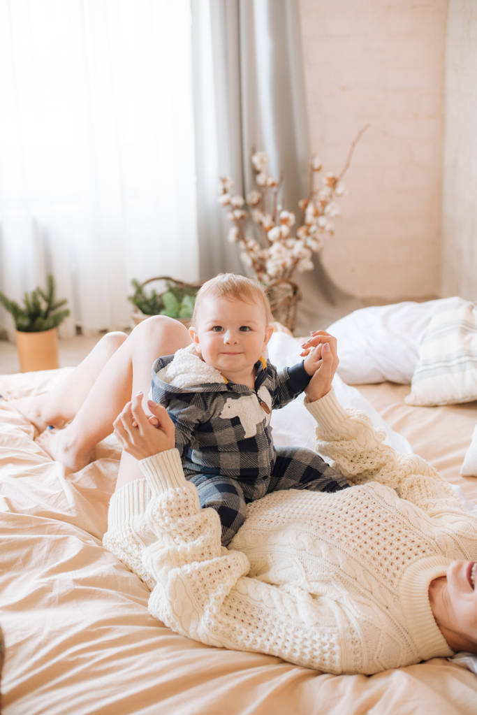 Fiatal anya és kisgyermek egy skandináv stílusú hálószoba díszített karácsonyi koszorúk és tűk egy nagy fényes ágy. Karácsonyi hangulat - Fotó, kép