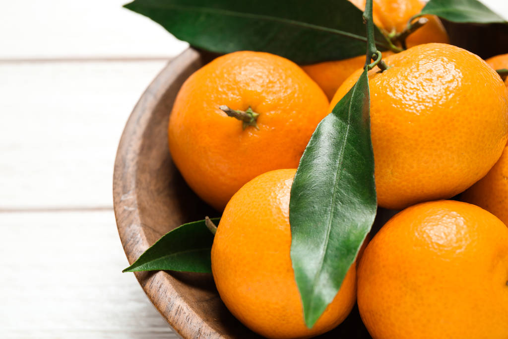 frische reife Mandarinen mit Blättern in Holzschale auf weißem Tisch, Nahaufnahme. Zitrusfrüchte - Foto, Bild