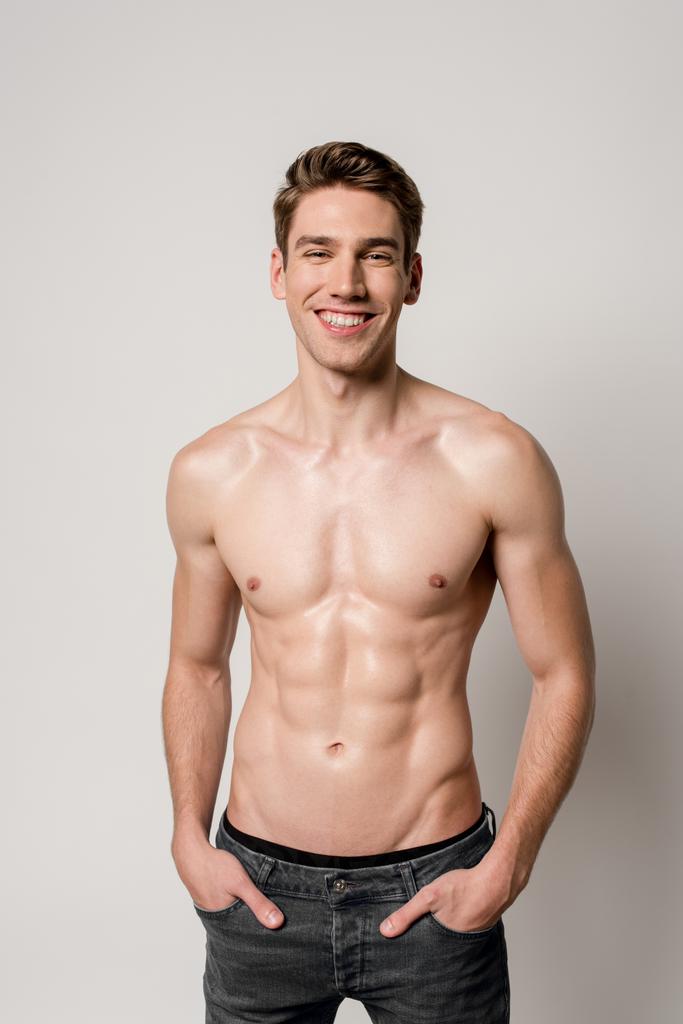 smiling sexy man with muscular torso with hands in pockets isolated on grey - Photo, Image