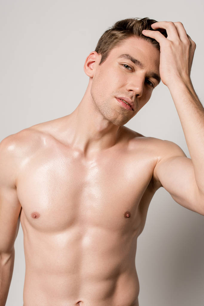 sexy muž s svalnatým trupem dotýkání vlasy izolované na šedé - Fotografie, Obrázek