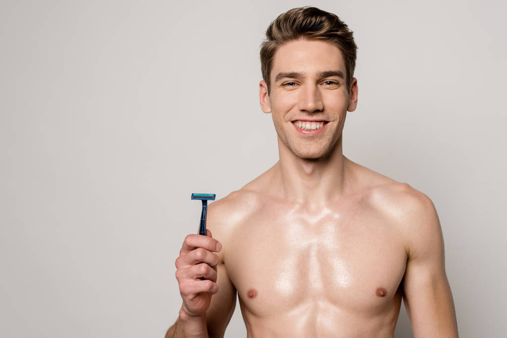усміхнений сексуальний чоловік з м'язистим торсом тримає бритву ізольовано на сірому
 - Фото, зображення