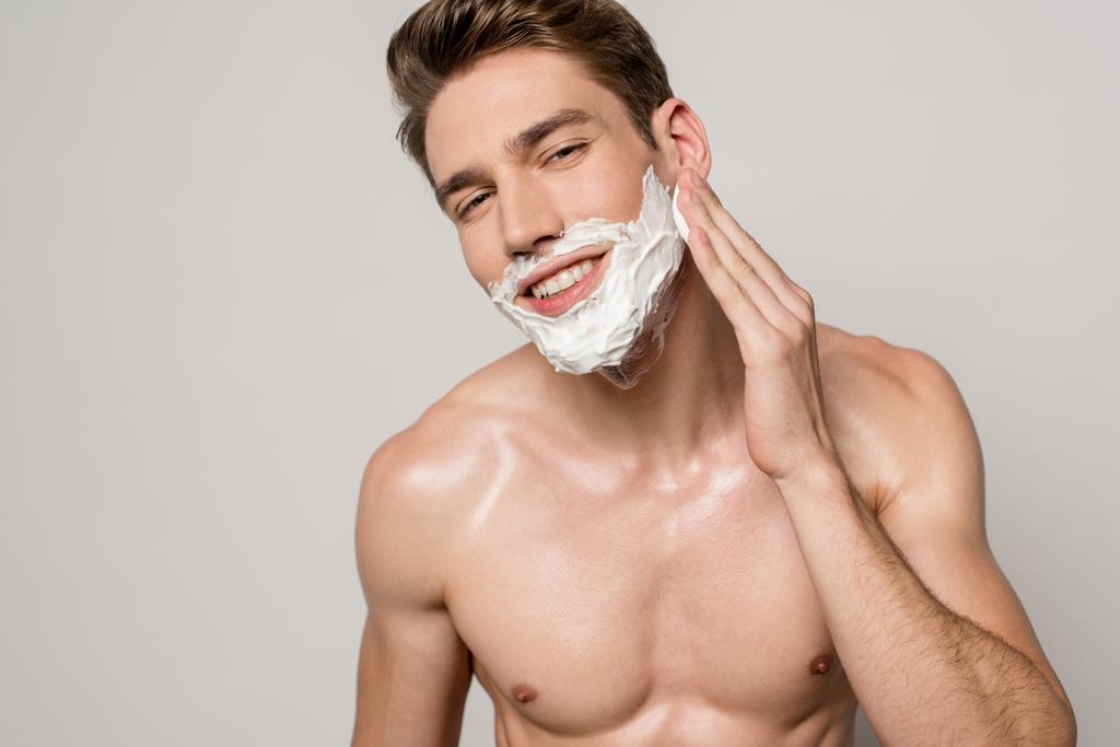 sorrindo homem sexy com torso muscular aplicando espuma de barbear isolado em cinza
 - Foto, Imagem