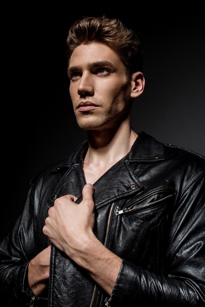 сексуальный молодой человек в байкерской куртке смотрит в сторону на черном фоне
 - Фото, изображение