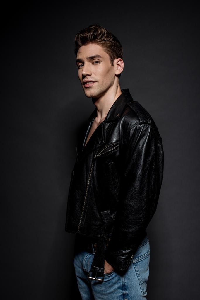 side view of handsome sexy young man in biker jacket on black background - Photo, Image