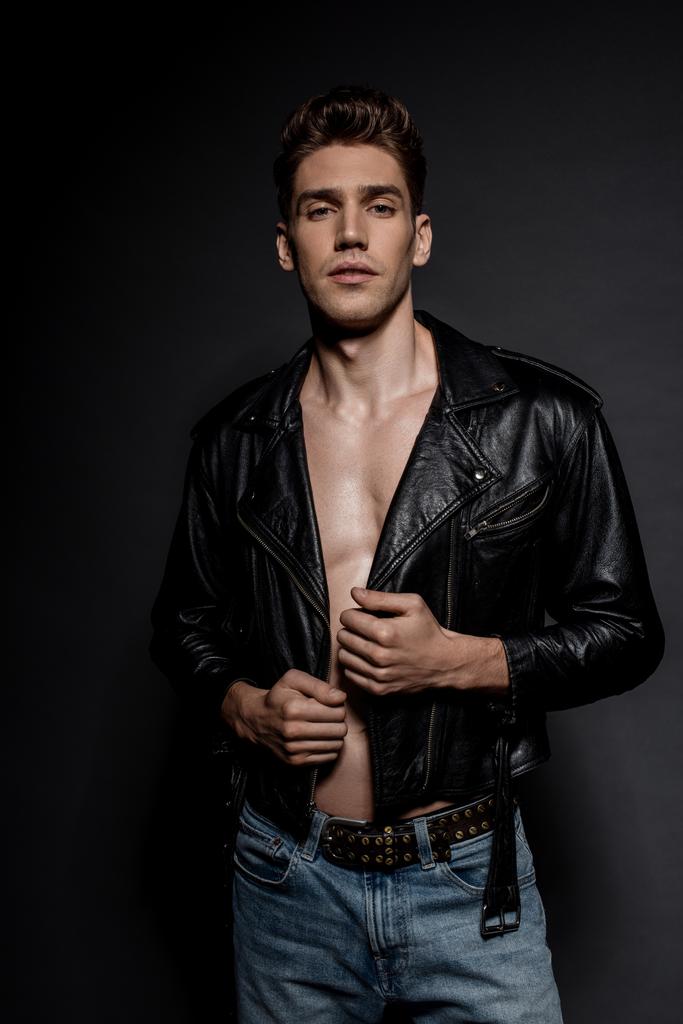 сексуальный молодой человек с мускулистым туловищем в байкерской куртке и джинсах на черном фоне
 - Фото, изображение
