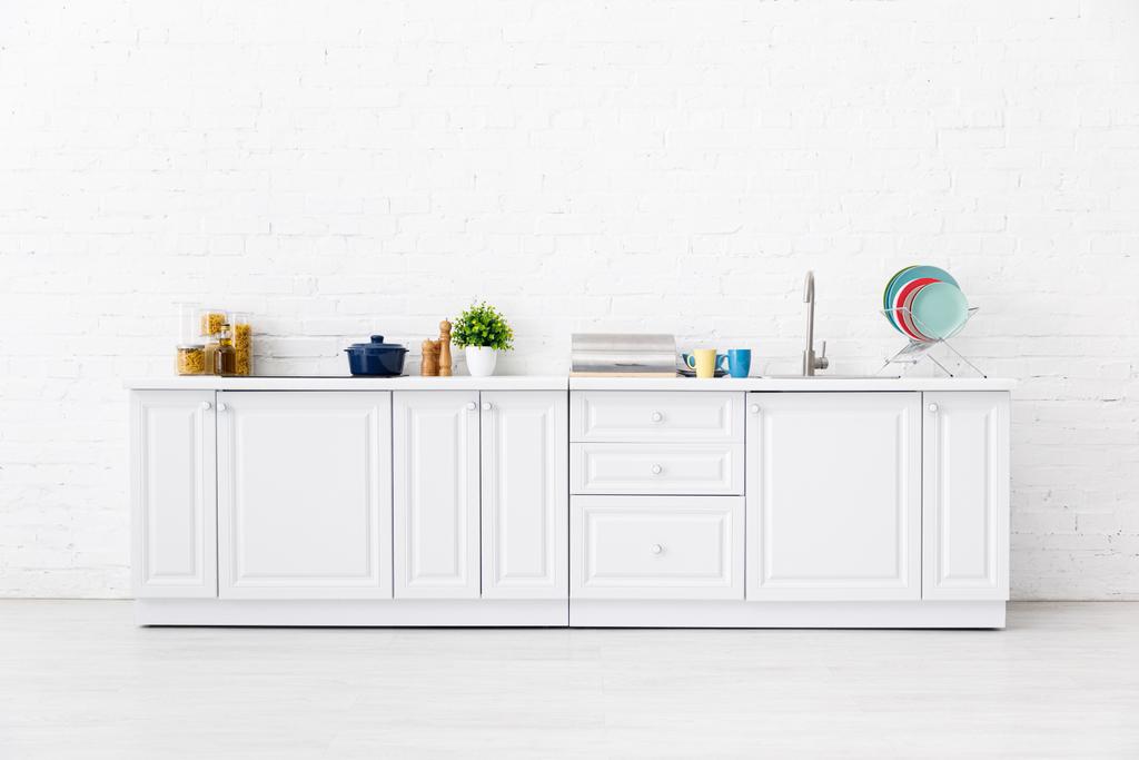 nowoczesne białe wnętrze kuchni z przyborami kuchennymi w pobliżu ściany z cegły - Zdjęcie, obraz