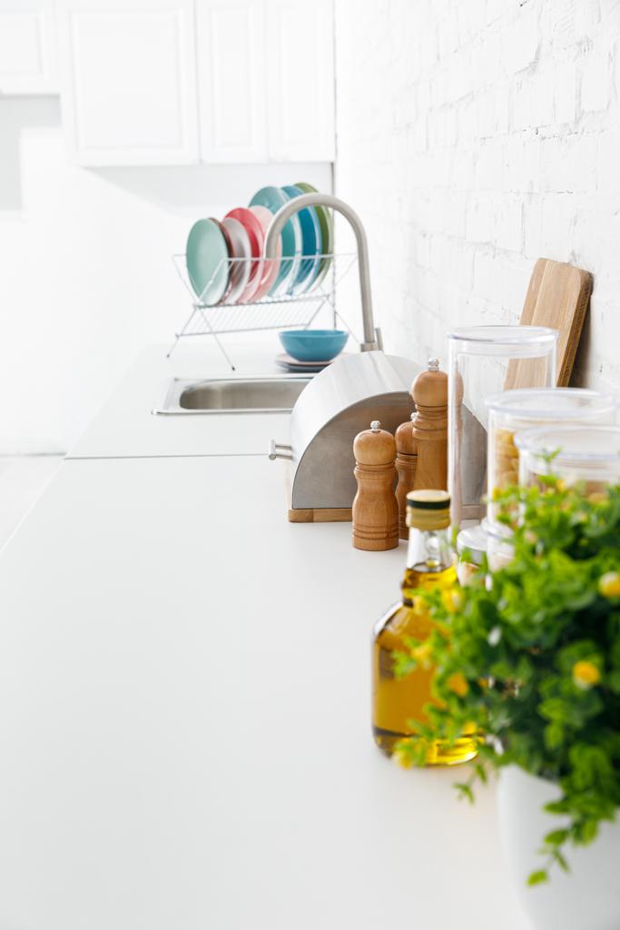 selectieve focus moderne witte keuken interieur met keukengerei en groene plant in de buurt van bakstenen muur - Foto, afbeelding