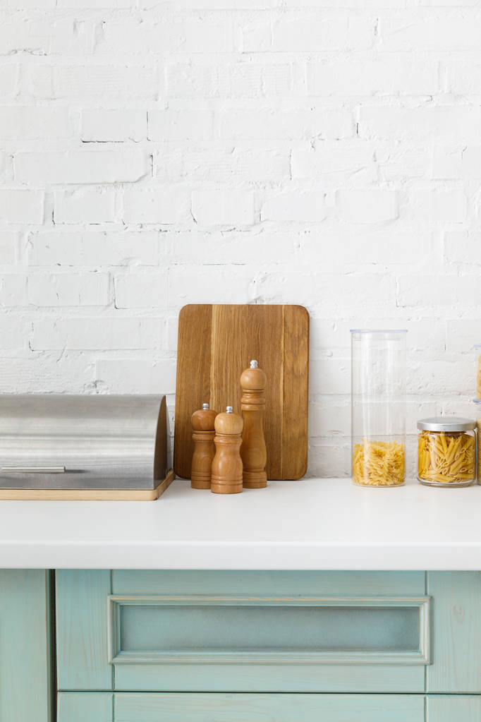 moderní bílý a tyrkysový kuchyňský interiér s nádobím, nádobím na jídlo a rostlinou u cihlové zdi - Fotografie, Obrázek