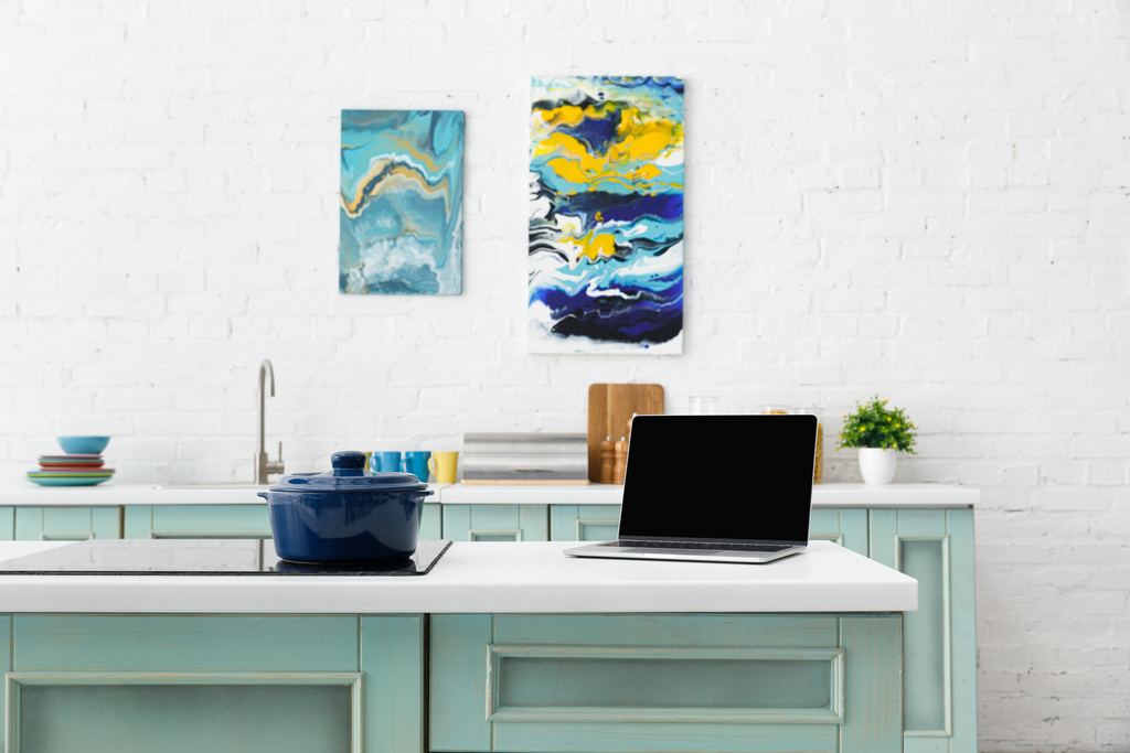 foyer sélectif de l'ordinateur portable et pot sur table de cuisson à induction avec ustensiles de cuisine et peintures abstraites sur fond
 - Photo, image