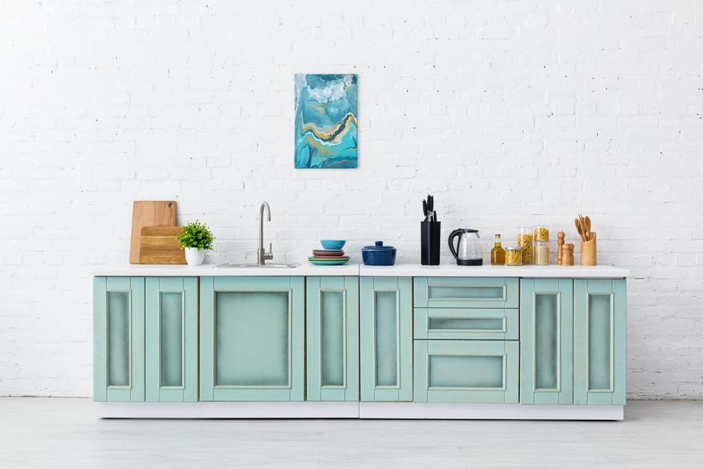 intérieur de cuisine blanc et turquoise avec ustensiles de cuisine et peinture abstraite sur mur de briques
 - Photo, image
