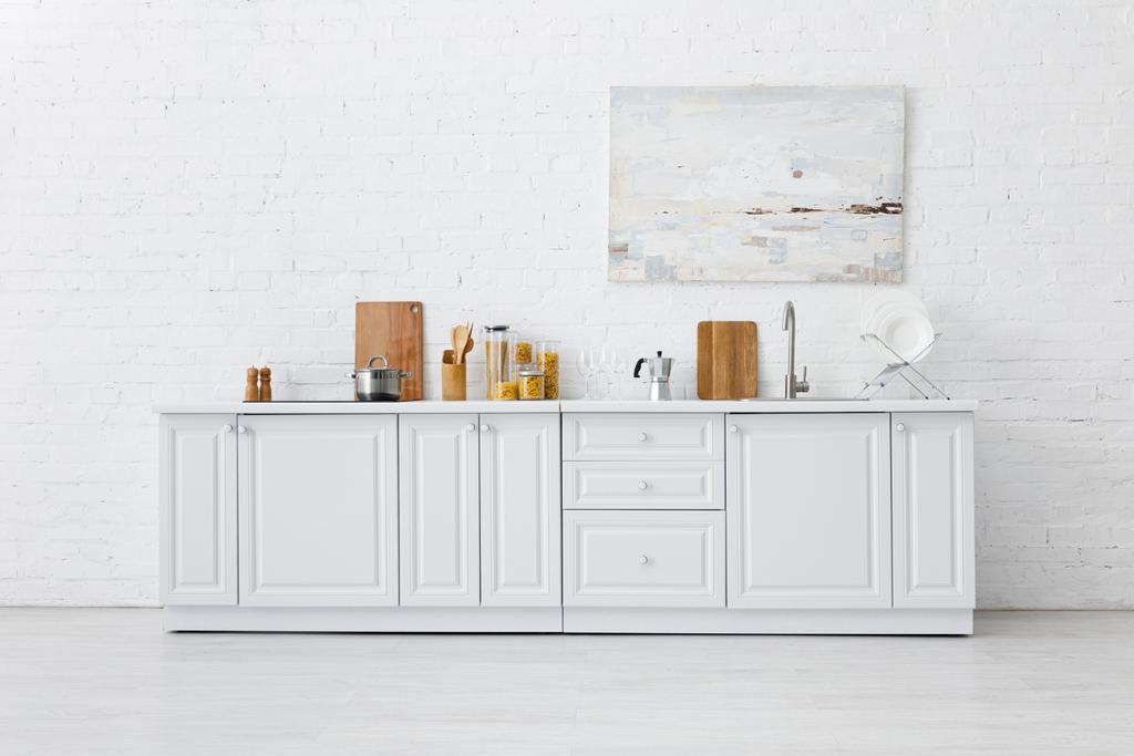 minimalistisches weißes Kücheninterieur mit Geschirr und Malerei an der Ziegelwand - Foto, Bild