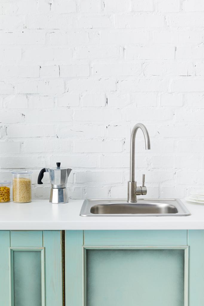 сучасний біло- бірюзовий інтер'єр кухні з посудом і раковиною біля цегляної стіни
 - Фото, зображення