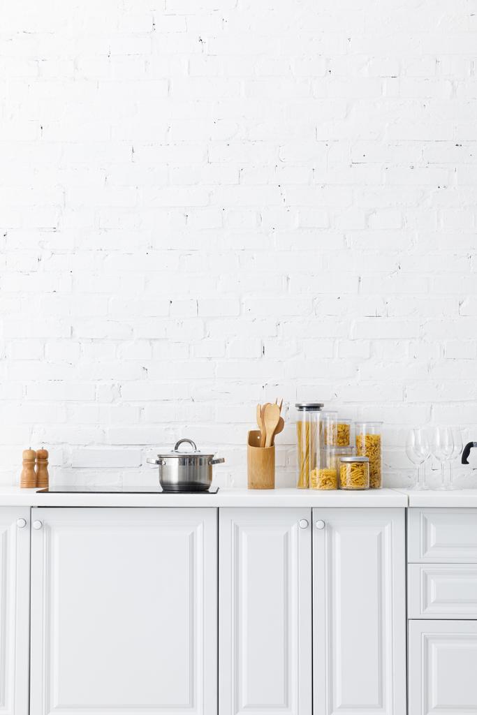 минималистичный современный белый интерьер кухни с кухонными принадлежностями и пищевыми продуктами возле кирпичной стены
 - Фото, изображение