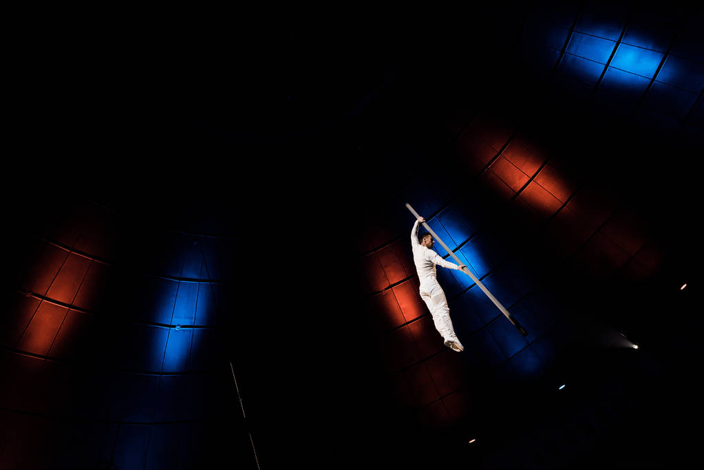 Blick auf den athletischen Akrobat, der auf einer Metallstange in der Manege des Zirkus balanciert  - Foto, Bild