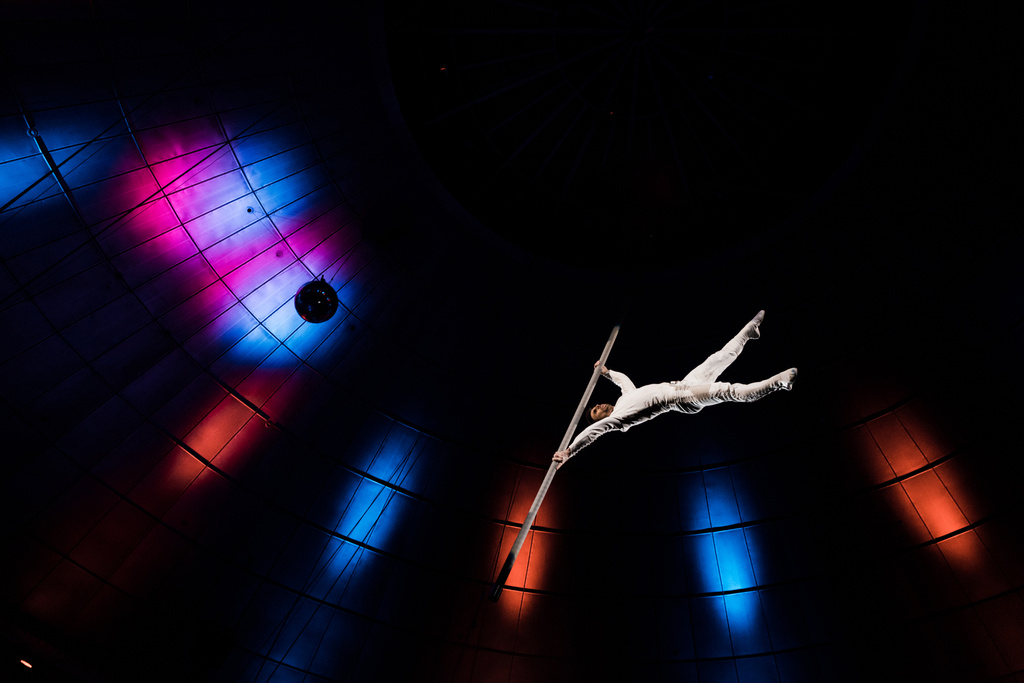 vista en ángulo bajo del acrobat atlético balanceándose en poste metálico cerca de la iluminación azul y roja en arena
 - Foto, Imagen