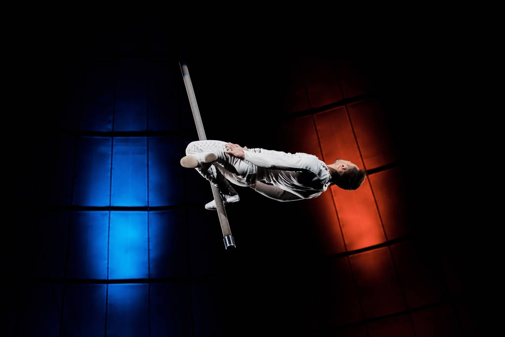 атлетический акробат балансирует на металлическом полюсе рядом с синим и красным освещением в цирке
  - Фото, изображение