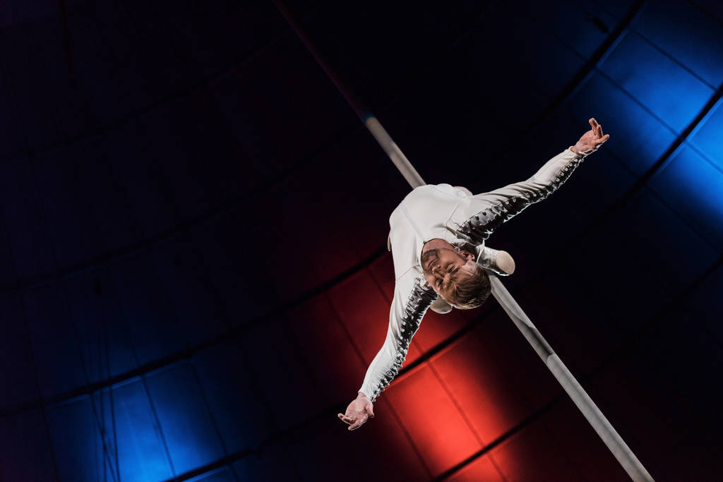 low angle view of strong acrobat with outstretched hands performing on metallic pole  - Photo, Image