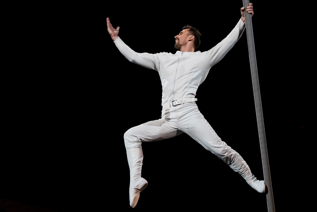 Starker Akrobat posiert während des Auftritts und hält metallische Stange isoliert auf schwarz  - Foto, Bild