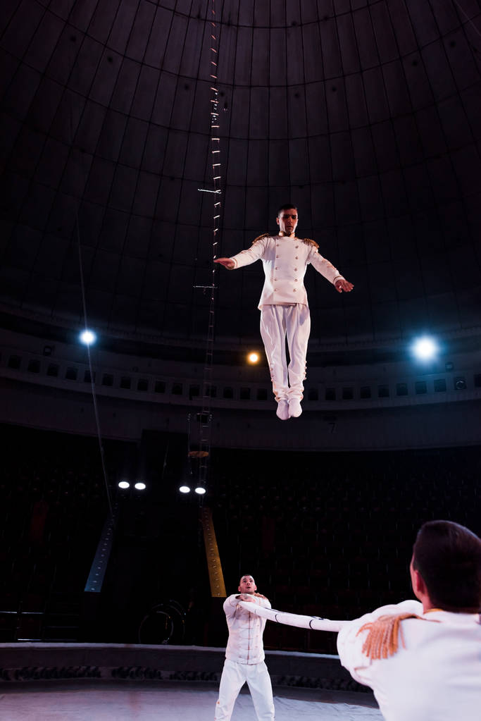 acrobats holding pole while handsome man jumping in circus  - Photo, Image