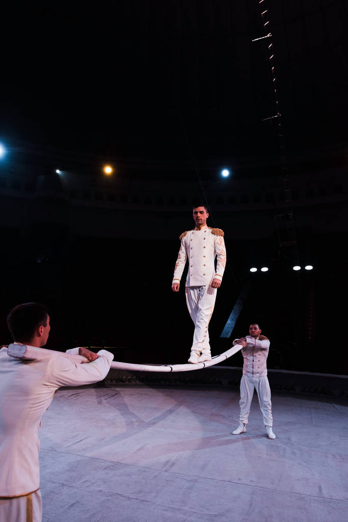acrobatas apoiando homem bonito andando sobre poste metálico no circo
  - Foto, Imagem