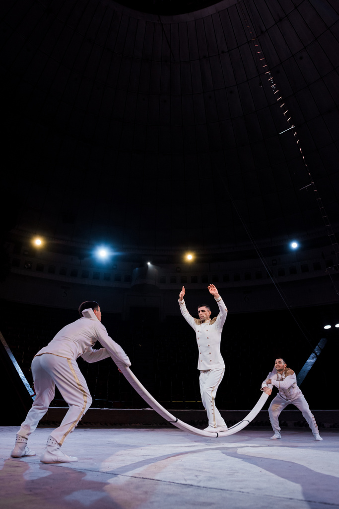 Akrobatlar, sirkte direğe atlamaya hazır ellerini uzatmış adamı destekliyor. - Fotoğraf, Görsel