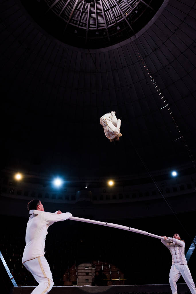 acrobaten houden paal en kijken naar turner springen in circus - Foto, afbeelding