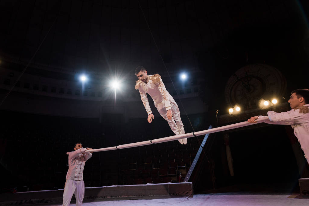 guapo gimnasta ejercitando en polo cerca de acróbatas en circo
 - Foto, Imagen