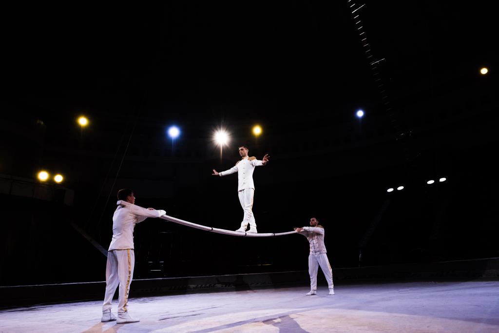Flexibler Luftakrobat balanciert auf Stange neben Männern im Zirkus  - Foto, Bild