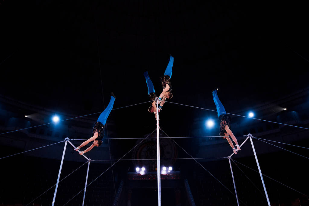 ginastas de visão de baixo ângulo atuando em bares horizontais na arena de circo
   - Foto, Imagem