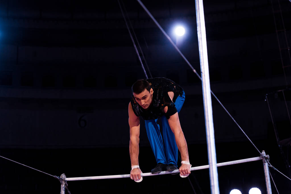 handsome gymnast performing on horizontal bars in arena of circus   - Photo, Image