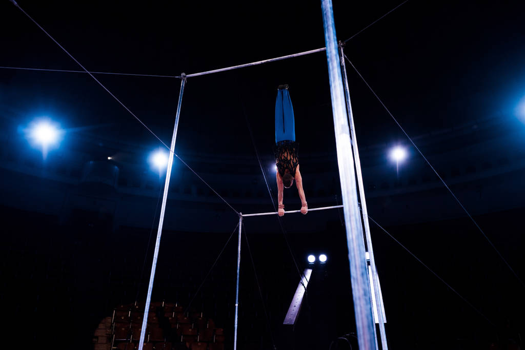 zadní pohled na akrobata vystupujícího na vodorovných tyčích v aréně cirkusu   - Fotografie, Obrázek