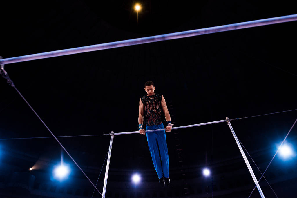 lage hoek van atletische turner presteren op horizontale balken in arena van circus   - Foto, afbeelding