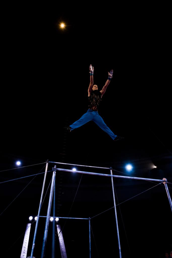 low angle view of gymnast jumping near horizontal bars in arena of circus   - Photo, Image
