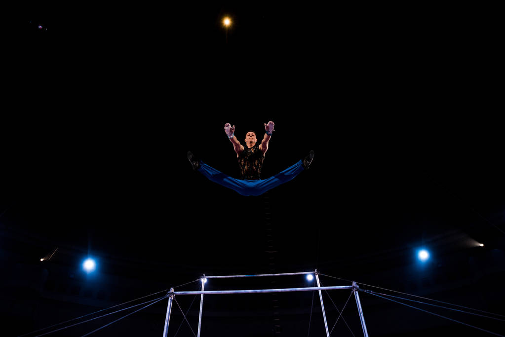  low angle view of gymnast jumping near horizontal bars while performing in circus   - Photo, Image