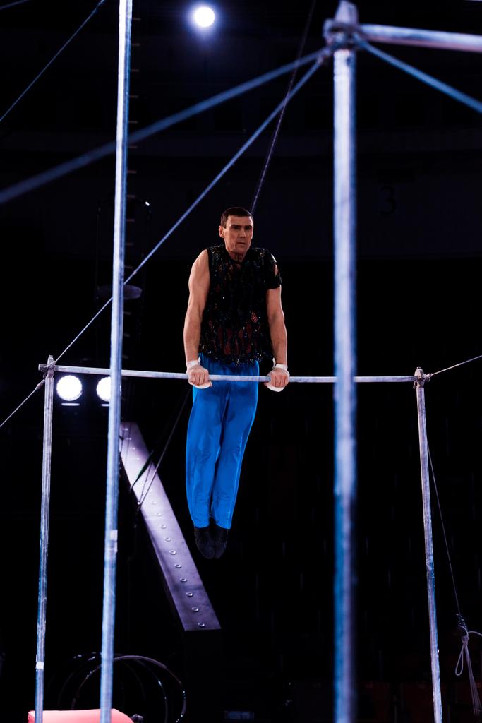 selective focus of handsome and strong gymnast performing on horizontal bars in arena of circus   - Photo, Image