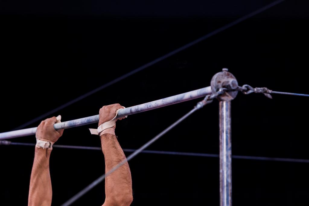 cropped view of athletic gymnast performing on horizontal bars in circus   - Photo, Image