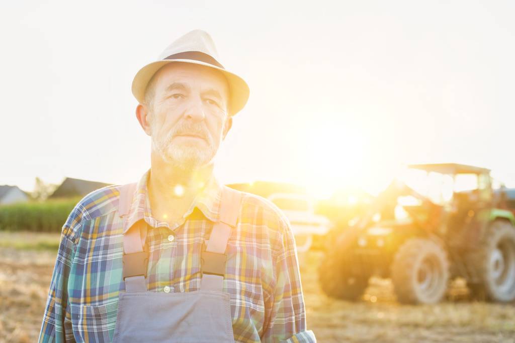 Портрет уверенного старшего фермера, стоящего против трактора на ферме
 - Фото, изображение