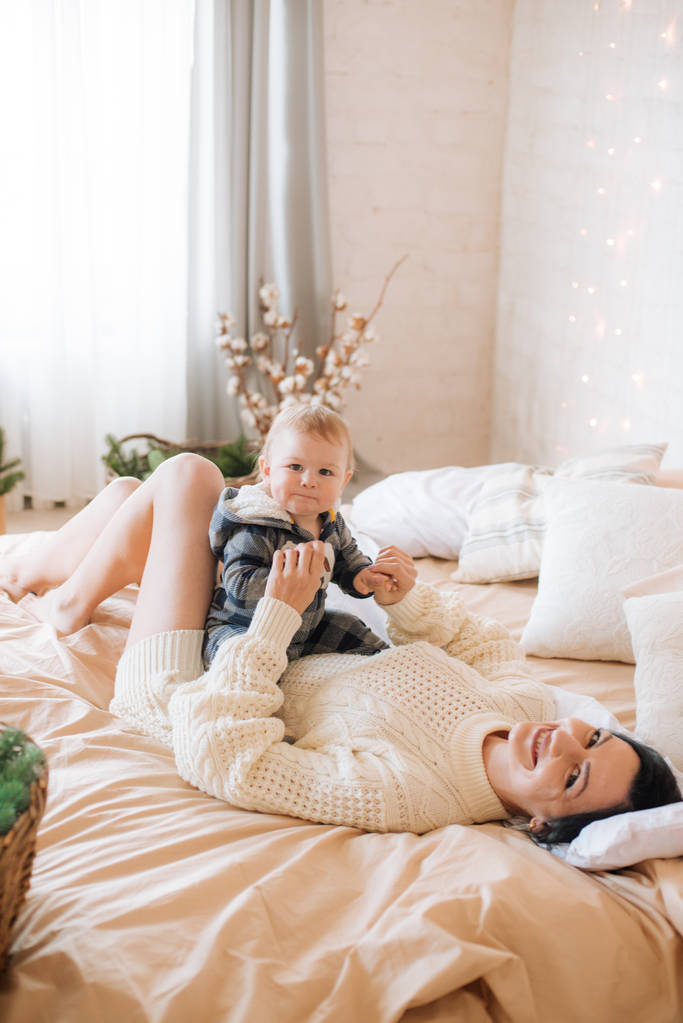 Молода мати і маленький син-малюк у скандинавській спальні, прикрашені різдвяними садами і голками на великому яскравому ліжку. Різдвяний настрій - Фото, зображення