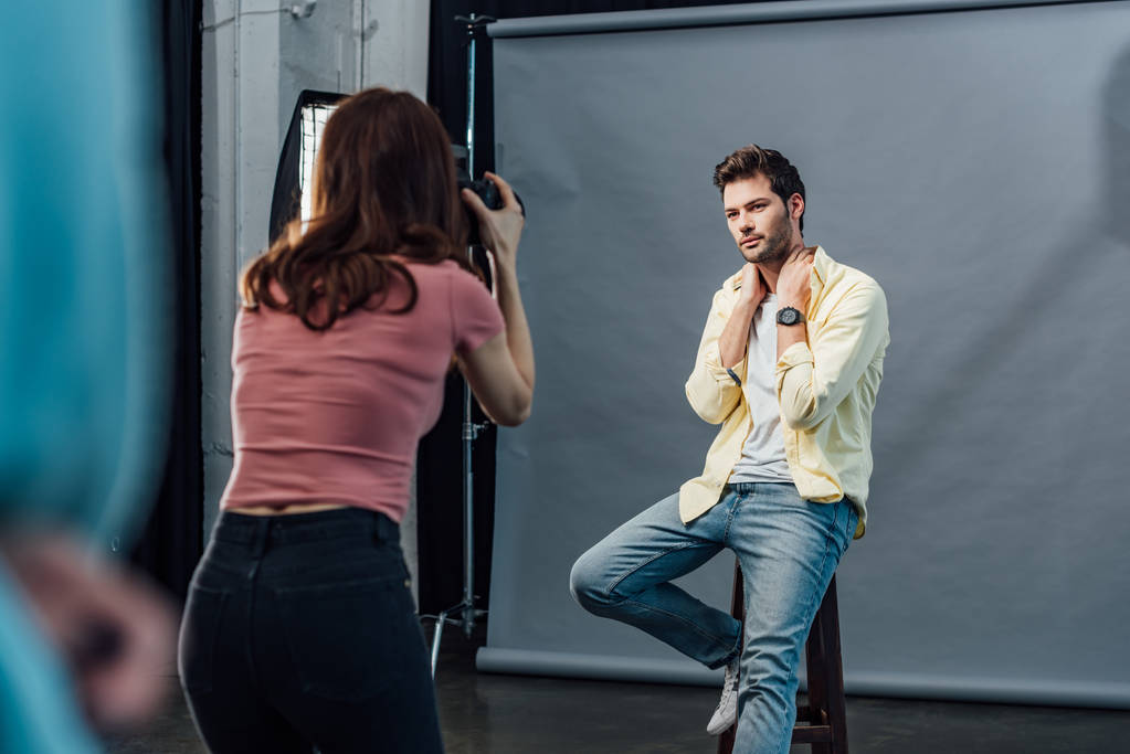 back view of photographer taking photo of handsome model posing while sitting on chair  - 写真・画像