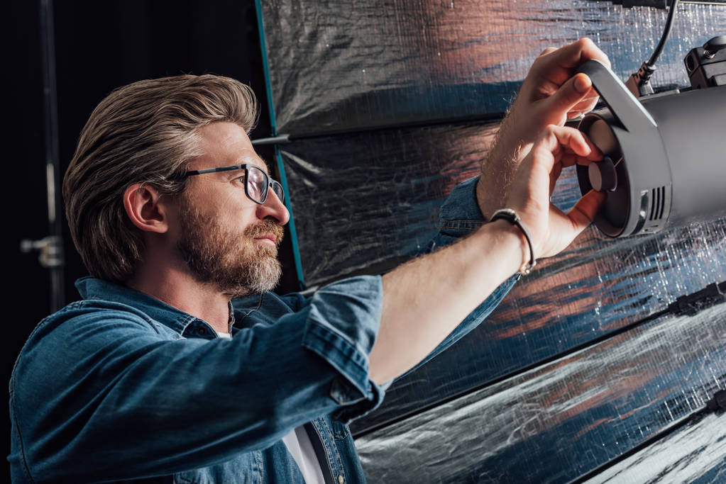 bearded art director touching reflector in photo studio  - 写真・画像
