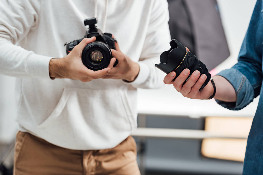 visão recortada do fotógrafo segurando câmera digital perto do diretor de arte com lente da câmera
  - Foto, Imagem