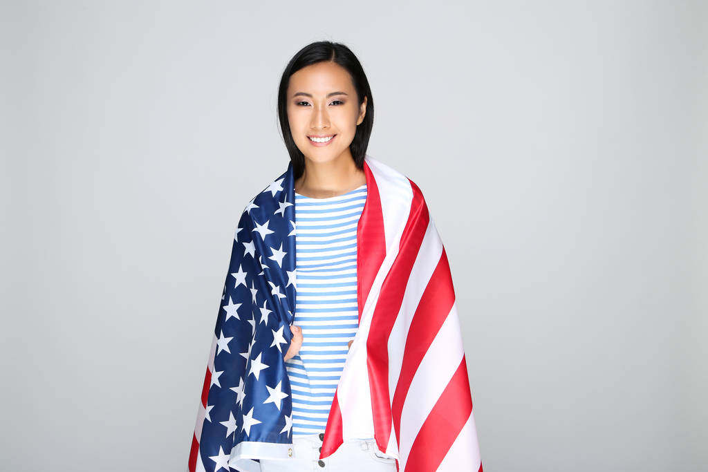 Mujer joven envuelta en bandera americana sobre fondo gris
 - Foto, imagen