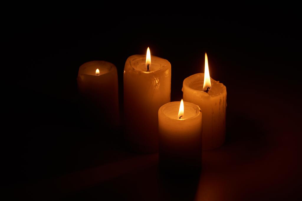 burning candles glowing in darkness on black background - 写真・画像